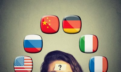 Work and travel immigration opportunity concept. Foreign language studying process. Woman with question mark and icons of international flags above head isolated on gray wall background.