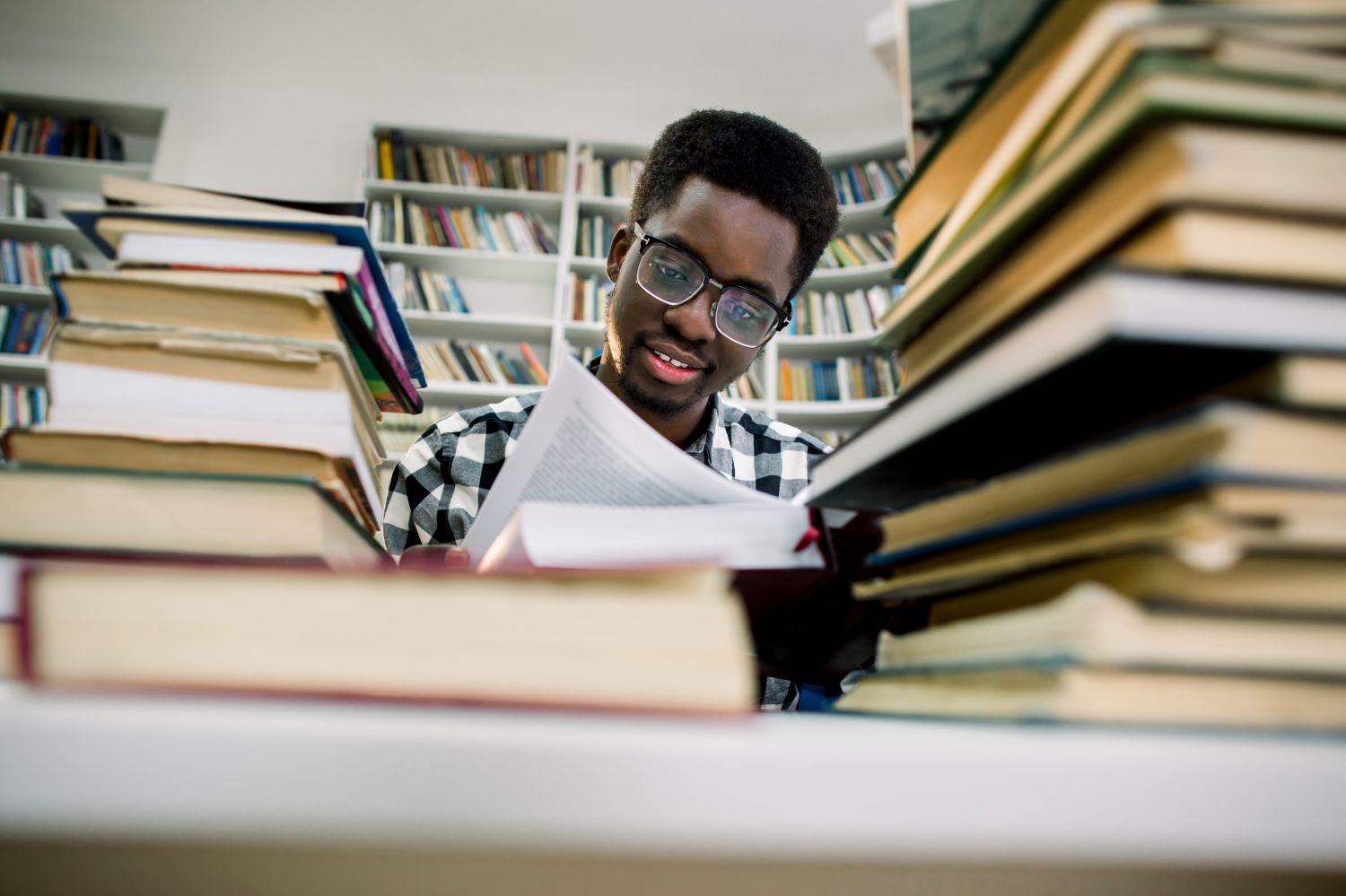 Cheerful dark skinned male student spending time on autodidact in library with book, positive african american hipster guy satisfied with interesting bestseller reading contemporary literature