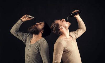 Company of dirty friends spend leisure with drinks. Men on drunk faces, dark background. Guys hold bottle and flask with alcohol,drinking. Alcohol addict concept. Alcohol, addiction, leisure