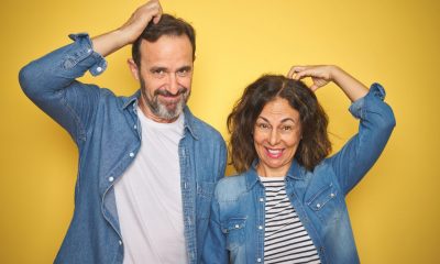 Beautiful middle age couple together wearing denim shirt over isolated yellow background confuse and wonder about question. Uncertain with doubt, thinking with hand on head. Pensive concept.