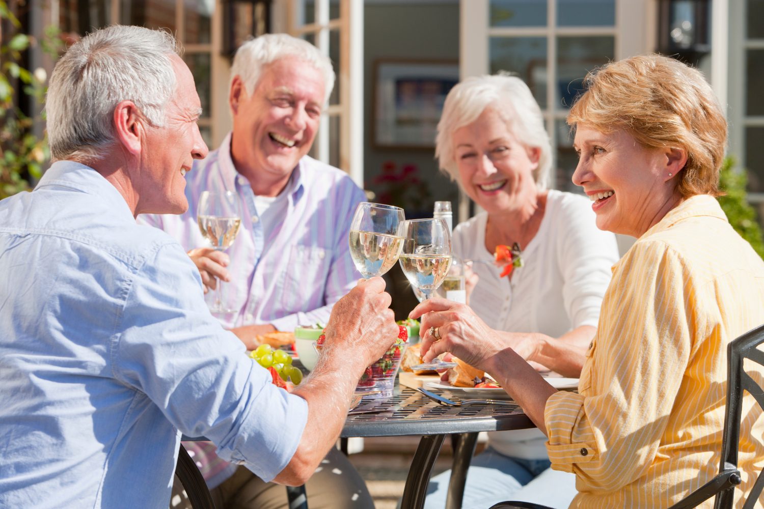 Medium shot of an elderly couple having lunch and toasting wine glasses at the patio table with friends.