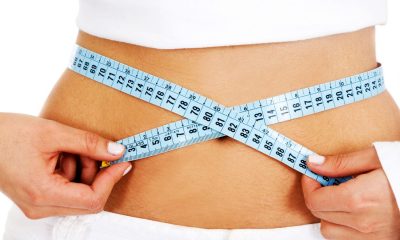 girl measuring her waist checking if she has had any weight loss - isolated over a white background