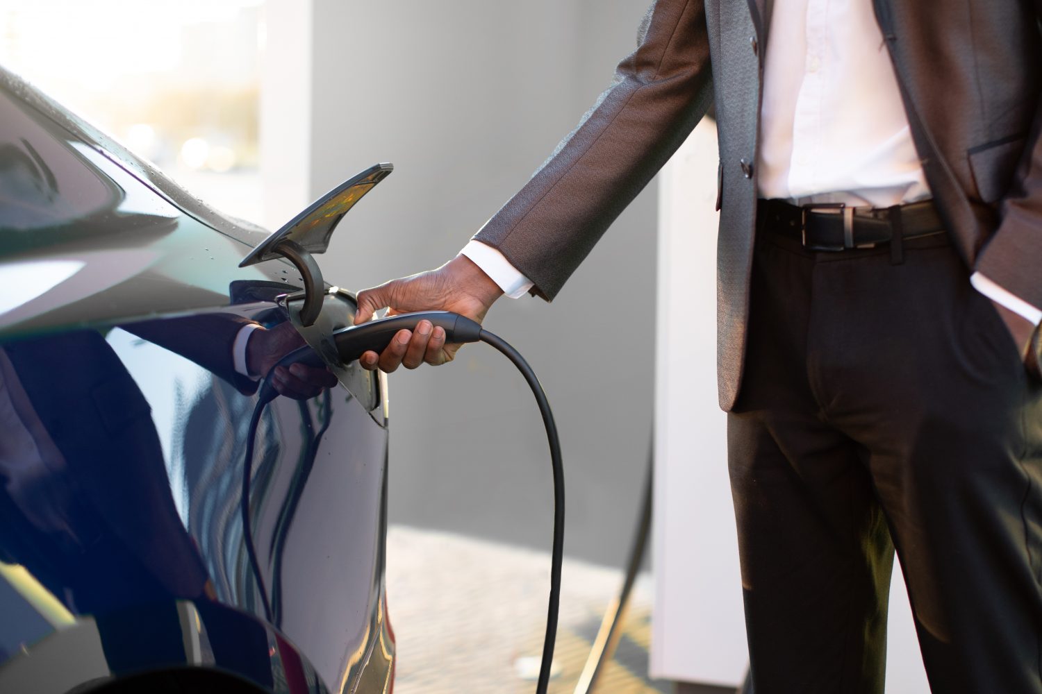 Lifestyle and ecology concept. Close up cropped image of young businessman recharging his luxury electro car