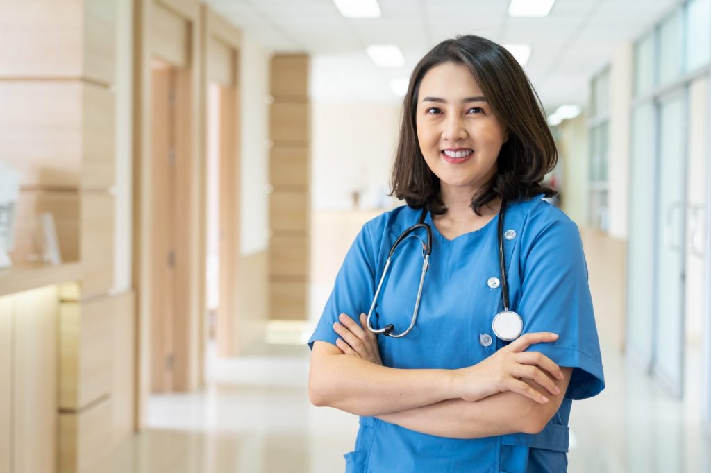 Portrait of Asian smiling female nurse in hospital corridor. Smiling woman doctor wear uniform in hospital corridor