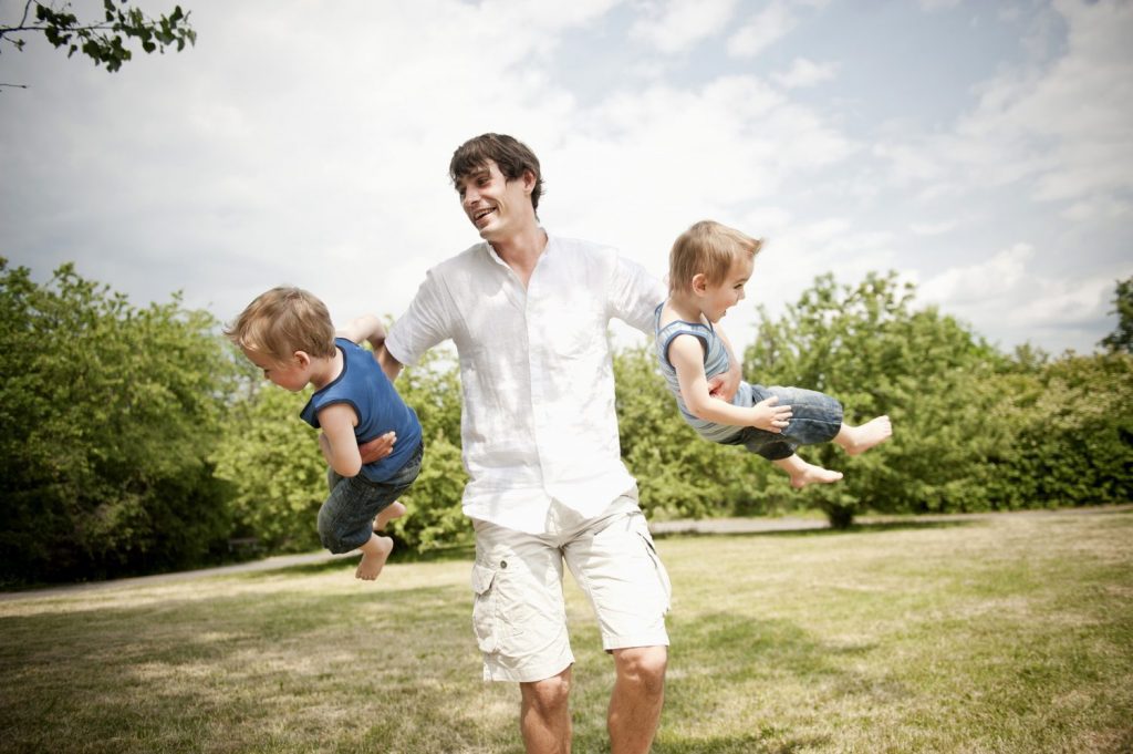 father spinning son's around in park