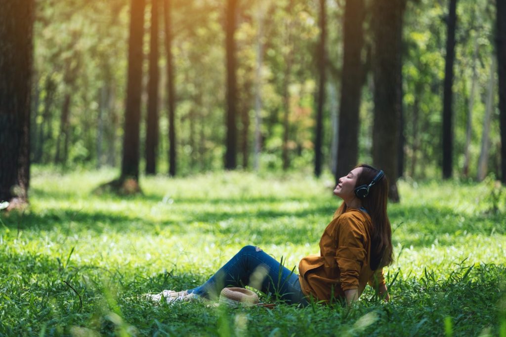 A beautiful young asian woman enjoy listening to music with headphone with feeling happy and relaxed in the park