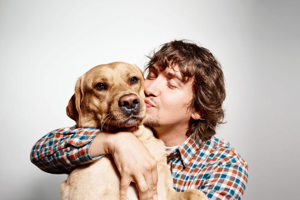 Closeup portrait handsome young hipster man, kissing his good friend dog isolated black grey background. Positive human emotions, facial expression, feelings.