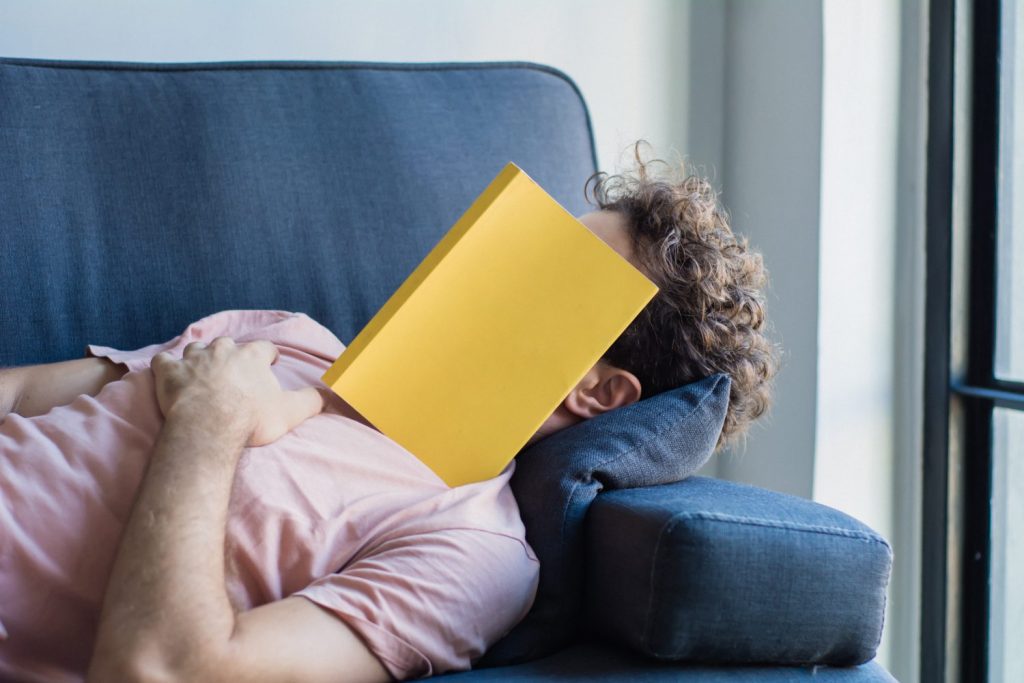 Young latin man sleep on sofa with book cover his face, sleep late reading book prepare for exam. Lifestyle education concept