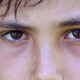 Serious angry child frowning to camera. Close-up of young boy staring macro eyes detail closeup