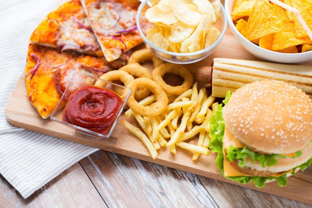 fast food and unhealthy eating concept - close up of hamburger or cheeseburger, deep-fried squid rings, french fries, pizza and ketchup on wooden table top view