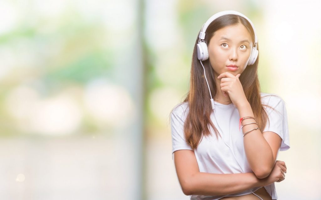 Young asian woman listening to music wearing headphones isolated background serious face thinking about question, very confused idea