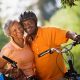 Active senior couple standing with bicycles in park, cheek to cheek, smiling, portrait (tilt)