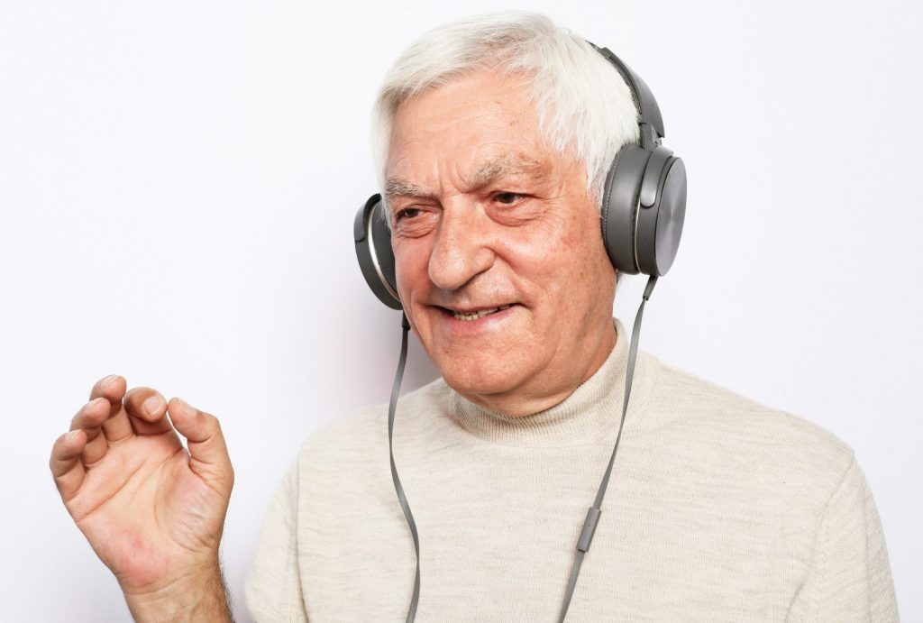 Lifestyle, tehnology and old people concept: image of an elderly gray-haired man listening to music with headphones over white background