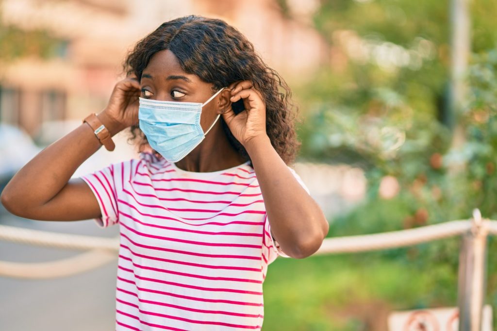 Young african american girl putting on protective medical mask standing at the park.