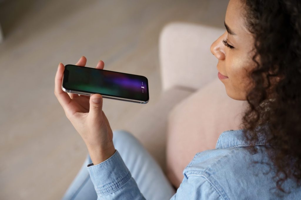 Young african woman user holding mobile phone in hand speak on speakerphone using virtual digital voice recognition assistant search on smartphone record audio message, mobile app ai tech assistance.