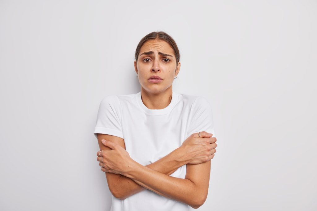 Scared worried European woman trembles from cold crosses arms over body needs something warm to wear stands freezing asks to turn headt on isolated over white background being not ready for winter