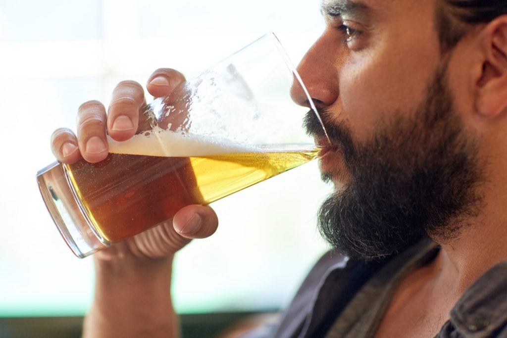 people, drinks, alcohol and leisure concept - close up of young man drinking beer from glass at bar or pub