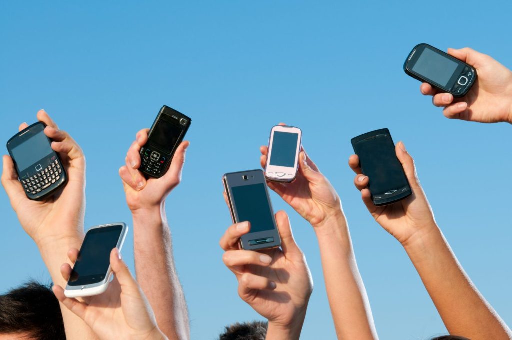 Happy people showing their modern mobile phones against blue sky